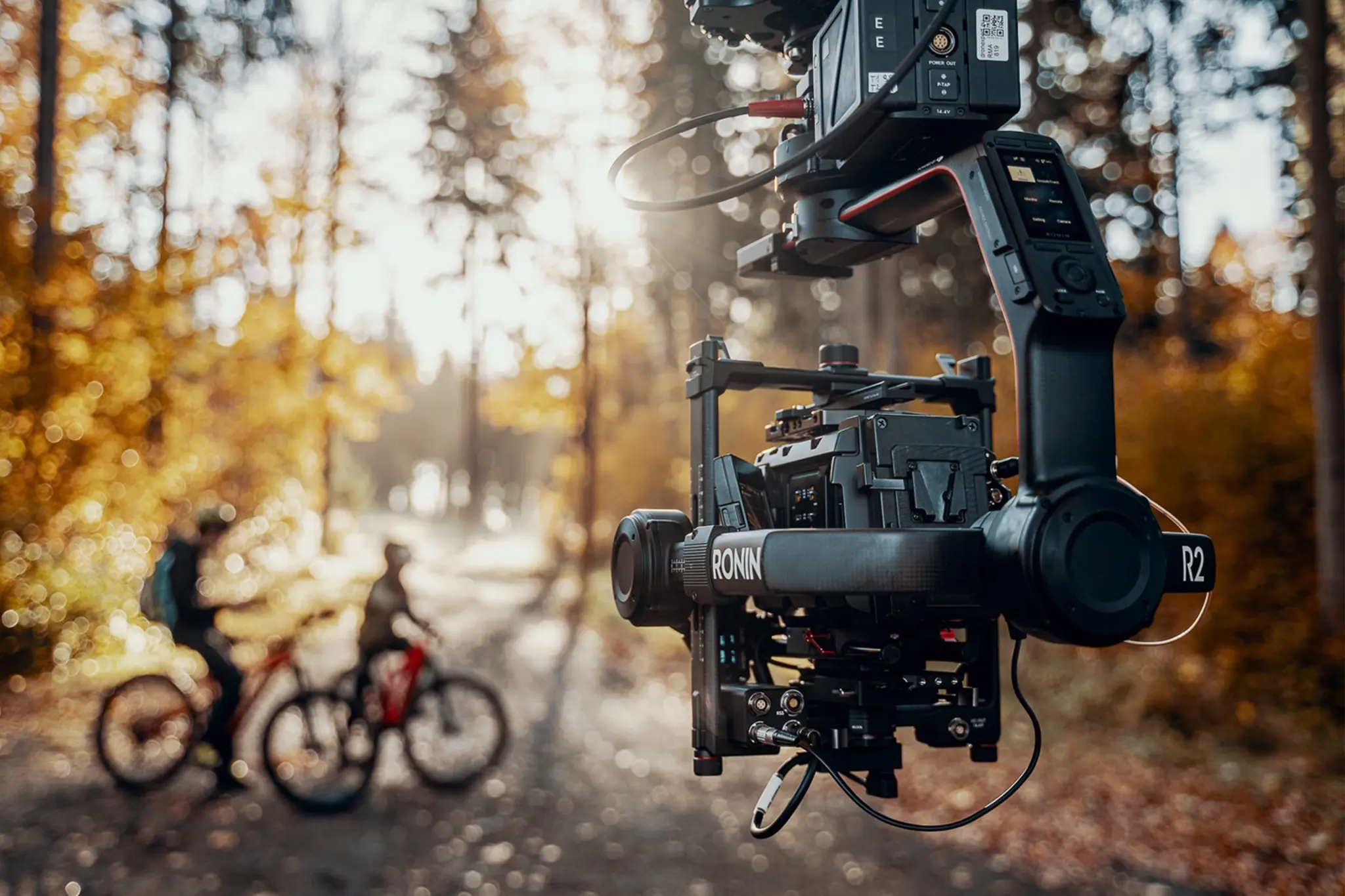 Packshot – kamera filmowa na gimbalu podczas nagrań w lesie, w tle rowerzyści | Packshot Warszawa